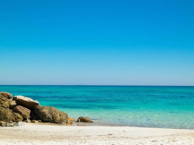 Vada sahilindeki taşlar, şeffaf, turkuaz su ve beyaz kum. Seyahat ve doğa kavramı.