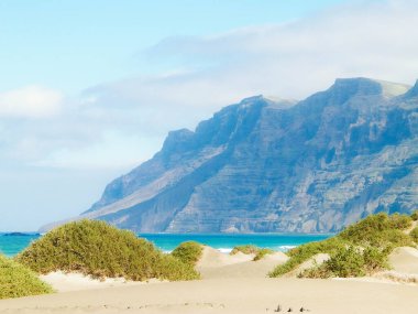 Plaj ve Dağlar - Caleta de Famara 'nın güzel kıyıları, Lanzarote Kanarya Adaları. Caleta de Famara 'daki plaj sörfçüler arasında çok popüler..
