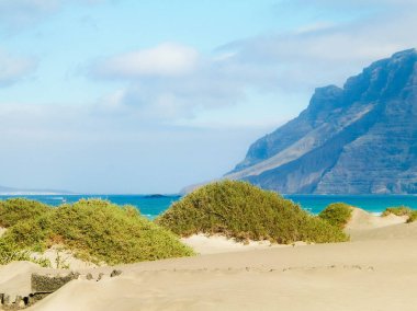Plaj ve Dağlar - Caleta de Famara 'nın güzel kıyıları, Lanzarote Kanarya Adaları. Caleta de Famara 'daki plaj sörfçüler arasında çok popüler..