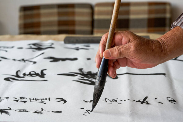 Старый китайский каллиграф пишет каллиграфические иероглифы, создавая каллиграфические работы