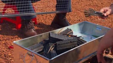 A group of people having a barbecue outdoors, burning charcoal in an oven to make a fire