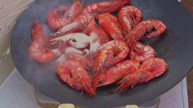 Group of prawns frying in a flat cast iron pan outdoors