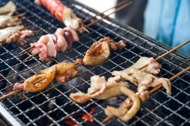 Bir grup insan dışarıda güçlü bir kömür ateşinin etrafında oturmuş ızgara yapıyor.