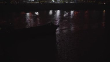 Büyük bir kum madeni gemisi gece şehir nehrinde yol alıyor.