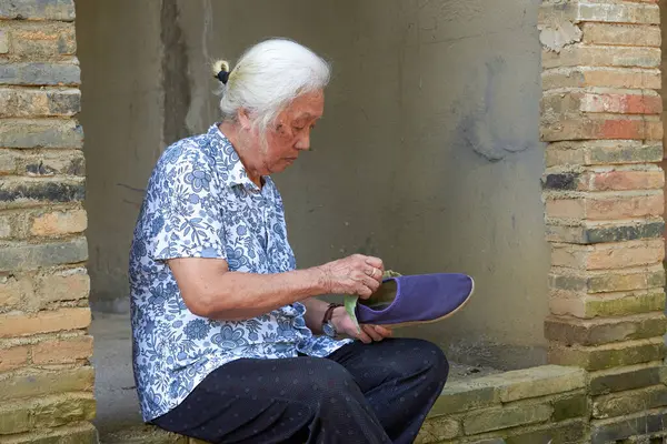 An old Asian grandmother is putting on shoes