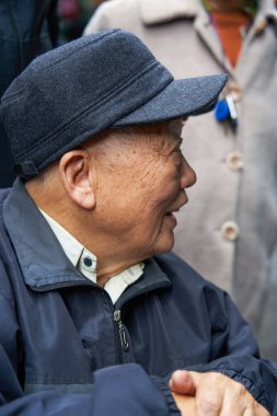 Yaşlı bir Asyalı adam markette şapka alır, seçer ve dener.