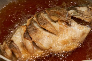 Mutfakta bir şef kızarmış balık yapıyor, bütün bir balığı kızartıyor.