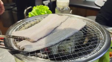 Kore barbekü restoranında çalışan biri kömür üstünde taze yılan balığı pişiriyor.