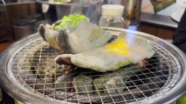 Kore barbekü restoranında çalışan biri kömür üstünde taze yılan balığı pişiriyor.