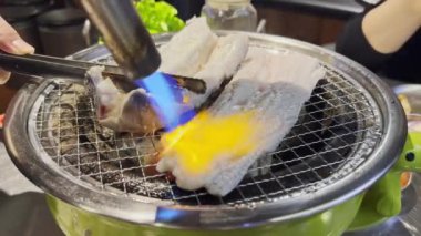 Kore barbekü restoranında çalışan biri kömür üstünde taze yılan balığı pişiriyor.