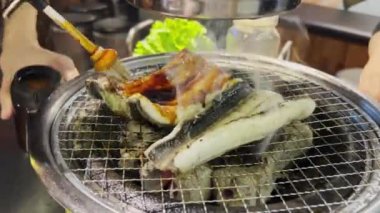 Kore barbekü restoranında çalışan biri kömür üstünde taze yılan balığı pişiriyor.