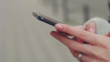 Genç bir kadının yakın çekimi akıllı telefonu elinde tutuyor ve haber yayınlarına aktarıyor. Kız elinin yakın çekimi şehir arka planında açık havada cep telefonu kullanıyor. Yüksek kalite 4k görüntü