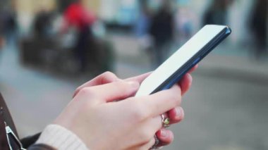 Genç bir kadının yakın çekimi akıllı telefonu elinde tutuyor ve haber yayınlarına aktarıyor. Kız elinin yakın çekimi şehir arka planında açık havada cep telefonu kullanıyor. Yüksek kalite 4k görüntü