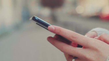 Genç bir kadının yakın çekimi akıllı telefonu elinde tutuyor ve haber yayınlarına aktarıyor. Kız elinin yakın çekimi şehir arka planında açık havada cep telefonu kullanıyor. Yüksek kalite 4k görüntü