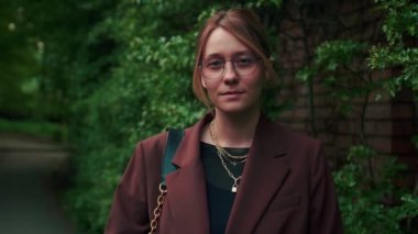 Gözlüklü, güpegündüz kameraya bakan, arka planda yeşil ağaçlar olan neşeli ve güzel beyaz bir kadın. Yüksek kalite 4k görüntü