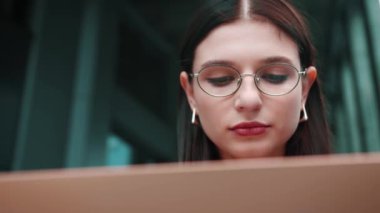 Bankta oturup dizüstü bilgisayar kullanmak. Resmi giyinmiş bir kadın iş binasının yakınında dışarıda. Yüksek kalite 4k görüntü