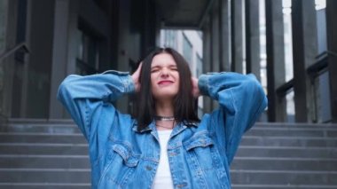 Güzel, modaya uygun bir model gülümser, açık havada poz verir ve uzun saçlarını düzleştirir. Açık şehir şehri. Yüksek kalite 4k görüntü