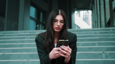 Güzel beyaz bir kadın, akıllı telefon kullanıyor, gülümseyen güzel bir kadın cep telefonu kullanıyor kameraya bakıyor ve gülümsüyor. Yüksek kalite 4k görüntü