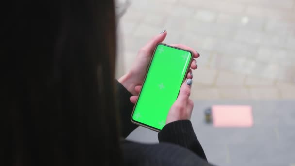 都会を背景に緑の画面の縦型携帯電話を持つ女性の手を閉じます スマートフォンでクロマキーモックアップ そうだ 高品質4K映像 — ストック動画