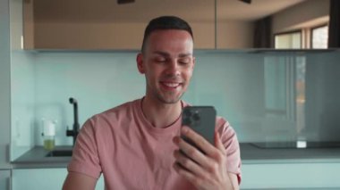 Serbest çalışan iş adamı akıllı telefondan evde video görüşmesi yapıyor. Kafkasyalı adam mutfakta oturup cep telefonuyla görüntülü konuşma yapıyor. Odaklanmış iş adamı el sallıyor.