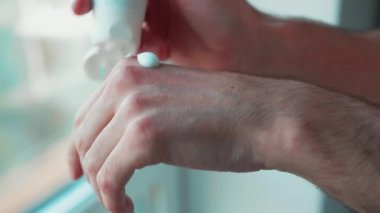 Erkek derisi. Erkek bakımı. Gömleksiz beyaz bir adam pencerenin yanında yumuşak el kremi sürüyor. Sıvı nemlendirici. Kozmetik ürünü. Metroseksüel yaşam tarzı. Yüksek kalite 4k görüntü