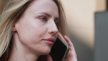 Odaklanmış iş kadını dışarıda cep telefonuyla konuşuyor. Akıllı telefondan konuşan gülümseyen kadın. Evde telefonda flört eden güzel bir kızın portresi. Yüksek kalite 4k görüntü