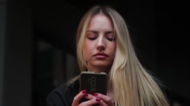 Genç, şık, beyaz bir kadının portresi. Akıllı telefonla konuşurken mesajlaşıyor ve sokakta gülümsüyor. Kapatın. Dışarı çıkın. Yüksek kalite 4k görüntü