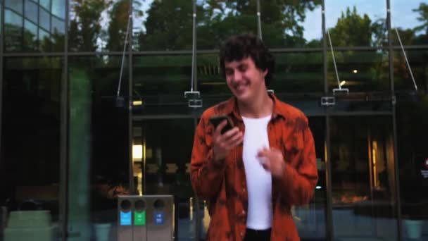 幸せなスタイリッシュなカジュアルな男は 電話で良いニュースを聞いてジャンプし オフィスビルの近くに屋外で幸せな感情で踊る 高品質4K映像 — ストック動画
