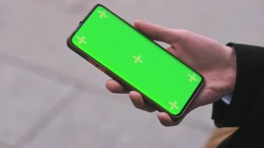 Mans Hand Holding Green Mock-Up Akıllı Telefon 'un yakın çekimi. Modern cep telefonu. Arka plandaki Cozy caddesinde. Yüksek kalite 4k görüntü