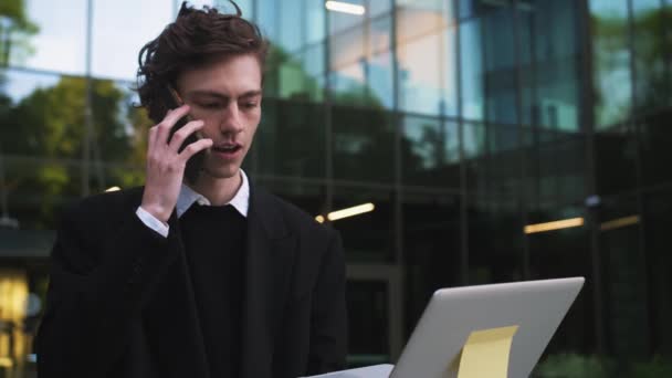 핸드폰으로 통화하는 젊은이는 노트북을 현대식 사무실 근처를 합니다 사업가가 통화를 — 비디오