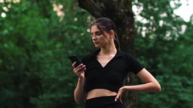 Kadın evde özel antrenör uygulaması olan akıllı telefon kullanıyor. Kadın spor yapmak için fitness uygulamasını kullanıyor. Yakın yörünge çekimi. Kadın spor yaparken cep telefonu kullanıyor. Yüksek