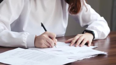 Genç beyaz kadın sözleşme imzalıyor, çalışan belgeleri ve çalışma ofisindeki anlaşma kağıdına yazı yazıyor, iş anlaşması ve resepsiyonist raporu hazırlıyor. Şirket sekreteri işini yapıyor.