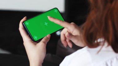 Akıllı telefon kullanan bir kadın cep telefonuyla yeşil ekran izliyor yatay oryantasyon kişisi evinde dinleniyor ve online eğlencenin tadını çıkarıyor. Yüksek kalite 4k görüntü