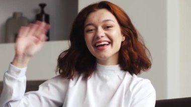 Genç, beyaz tenli, hipster video blogger kadın kameraya el sallıyor kamerayla konuşuyor masa başında video konferansında sosyal mesafe arkadaşıyla sanal sohbet görüşmesi yapıyor. Yüksek kalite 4k
