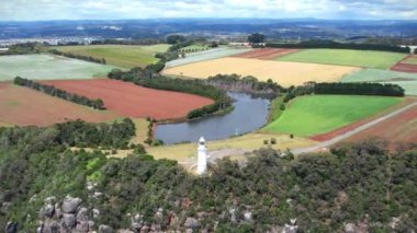 Kıyı uçurumundaki beyaz deniz feneri ve Tasman Denizi 'nin renkli tarlalarında bir göl yukarıdan görünüyor..