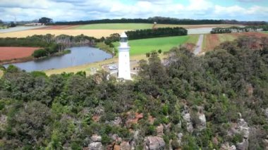 Kıyı uçurumundaki beyaz deniz feneri ve Tasman Denizi 'nin renkli tarlalarında bir göl yukarıdan görünüyor..