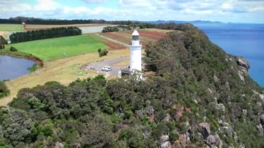 Kıyı uçurumundaki beyaz deniz feneri ve Tasman Denizi 'nin renkli tarlalarında bir göl yukarıdan görünüyor..