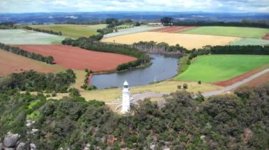 Kıyı uçurumundaki beyaz deniz feneri ve Tasman Denizi 'nin renkli tarlalarında bir göl yukarıdan görünüyor..