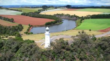 Kıyı uçurumundaki beyaz deniz feneri ve Tasman Denizi 'nin renkli tarlalarında bir göl yukarıdan görünüyor..