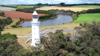 Kıyı uçurumundaki beyaz deniz feneri ve Tasman Denizi 'nin renkli tarlalarında bir göl yukarıdan görünüyor..