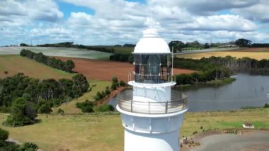 Kıyı uçurumundaki beyaz deniz feneri ve Tasman Denizi 'nin renkli tarlalarında bir göl yukarıdan görünüyor..