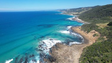 Okyanus dalgaları Avustralya kıyılarında turkuaz zümrüt renkli suyla beyaz bir kumsalda kırılıyor.