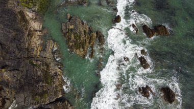 Kelt Denizi 'nin kayalık sahillerinde dalgalar kopuyor. Deniz dalgalarında beyaz köpük. Atlantik 'in kıyı şeridi. Turkuaz deniz suyu. Nefes kesici deniz manzarası.