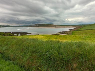 Deniz koyunun yakınındaki tepede sık yeşil çimenler. Clonakilty Körfezi üzerinde bulutlu bir gökyüzü, deniz manzarası. Drone bakış açısı.