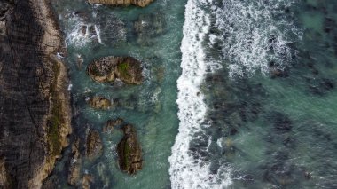 Kelt Denizi 'nin kayalık sahillerinde dalgalar kopuyor. Dalgalarda beyaz köpük. Atlantik 'in kıyı şeridi. Turkuaz deniz suyu. Nefes kesici deniz manzarası. Hava fotoğrafı. Yukarıdan görüntüle.