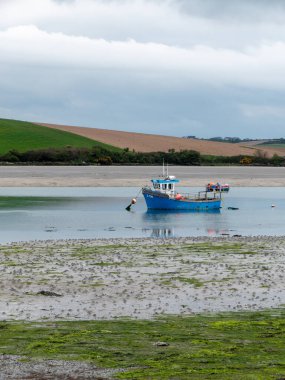 Bir gün gelgitte sığ sularda bir tekne. Bulutlu bir gökyüzünün altındaki tepeler. Çamur ve yosun. Peyzaj.