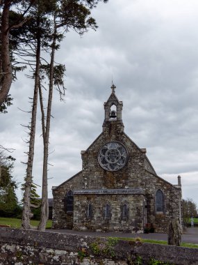 Bulutlu bir günde Taş Katolik Kilisesi. Hıristiyan dini bir bina, bulutların altındaki ağaçların yanındaki kilise..