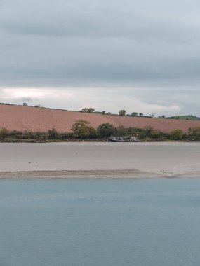 Kumsal kıyısı. Sakin su. Kıyıdaki eski gemi. Tarlaya sürülmüş. Minimalist manzara.