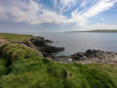 Güneşli bir günde Kelt Denizi 'nin resimli körfezi. İrlanda 'nın kayalık kıyıları. Deniz Burnu. Mavi gökyüzü, denizin üzerinde beyaz bulutlar.