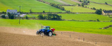 County Cork, İrlanda, 20 Ağustos 2022. Bir yaz günü İrlanda 'da mavi bir traktör sürülen bir tarlayı eker. İrlanda 'da bir çiftlikte tarım işi, tarım arazisi, tarlada traktör..